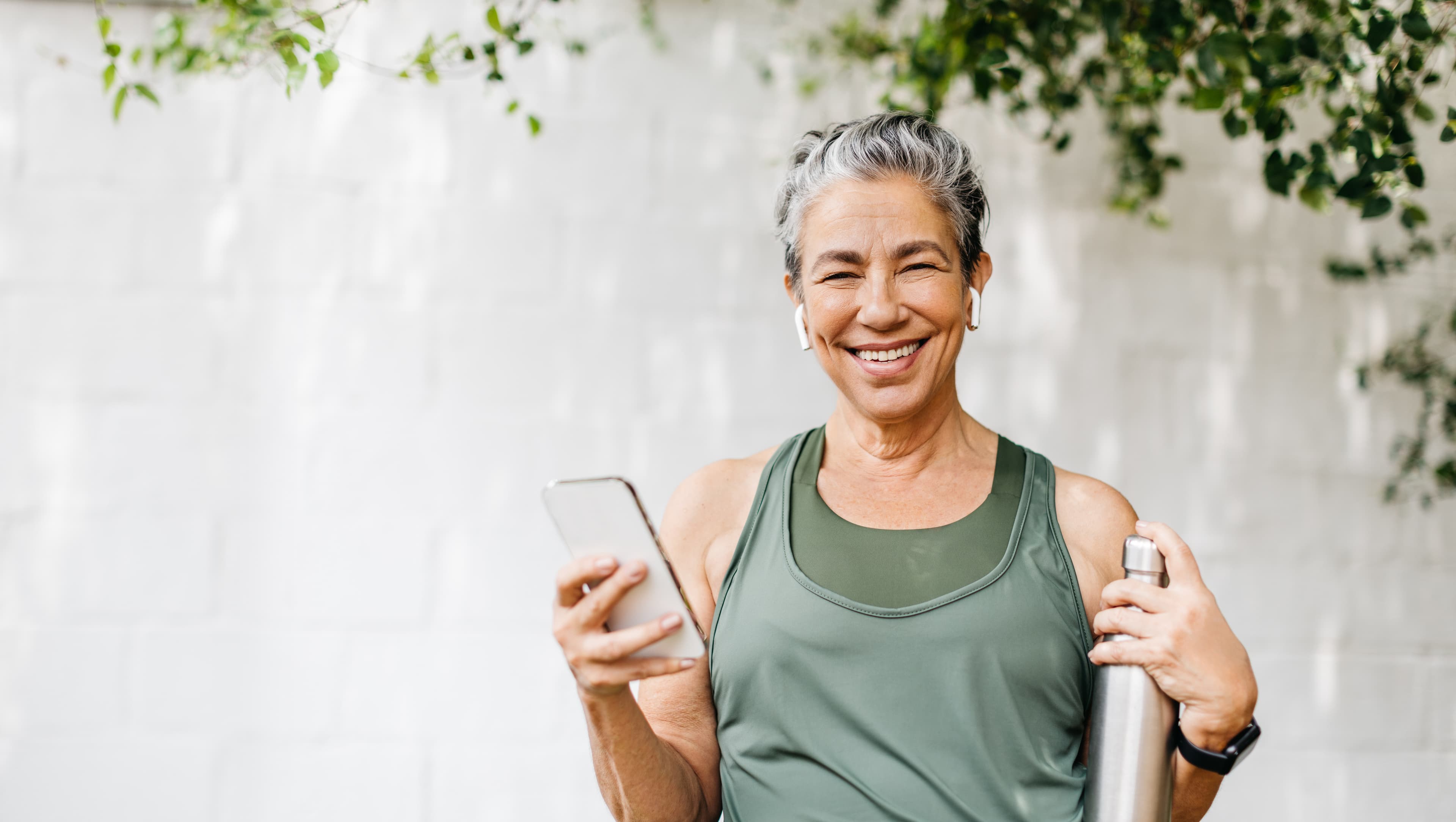 A smiling woman in workout clothes holding her phone and a water bottle, checking in with Daili