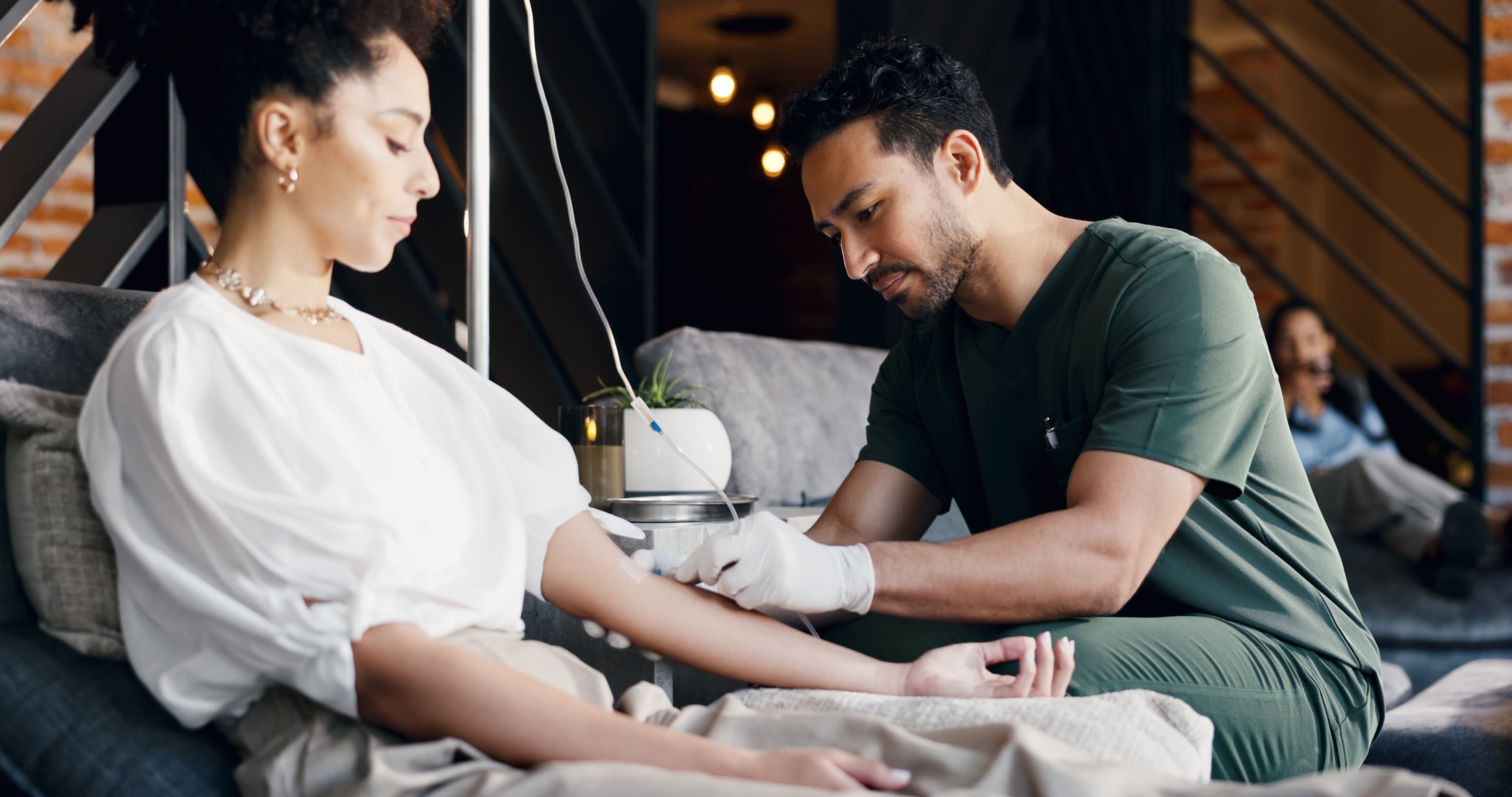 A wellness practitioner administering IV therapy to a relaxed client in a warm, modern treatment lounge